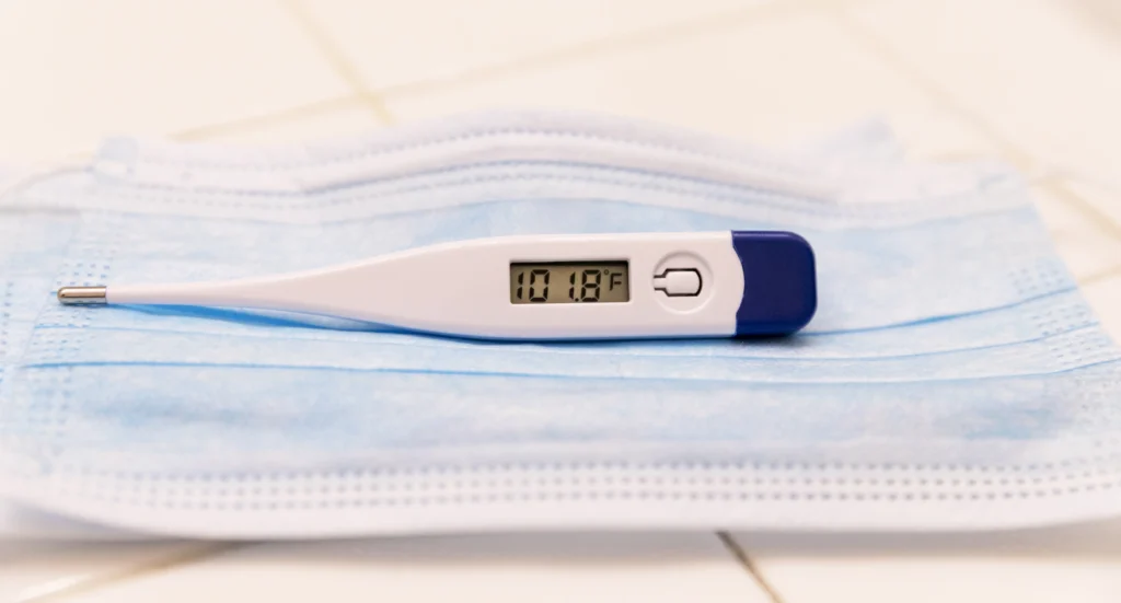 Person checking a thermometer while feeling unwell.